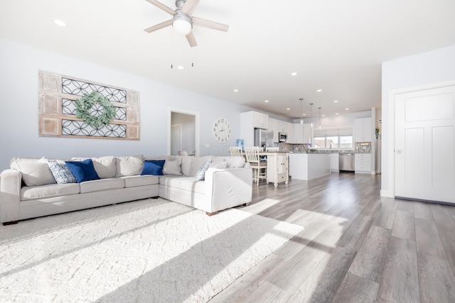 living room with light wood-type flooring, ceiling fan, and sink