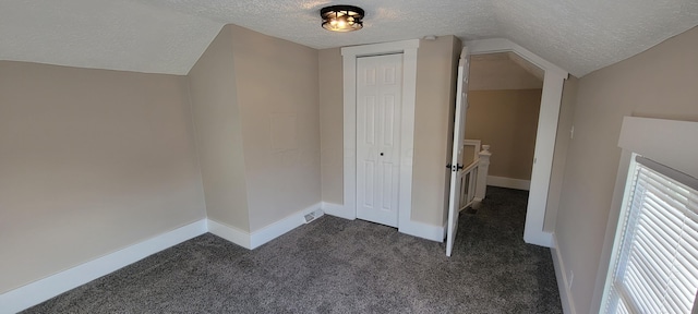 additional living space with vaulted ceiling, dark carpet, and a textured ceiling