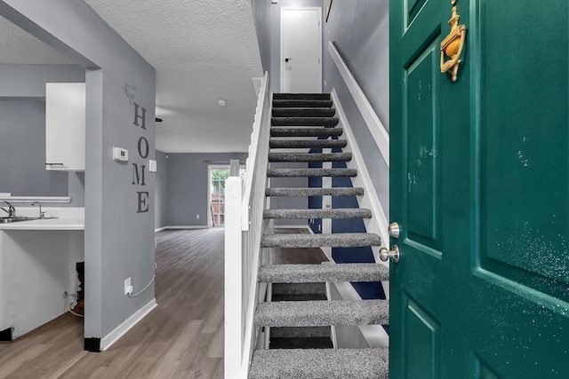 stairway with sink, wood-type flooring, and a textured ceiling