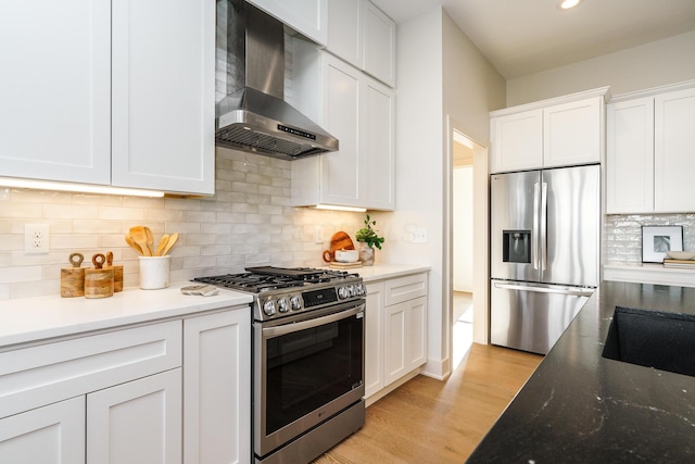 kitchen featuring appliances with stainless steel finishes, light hardwood / wood-style flooring, white cabinetry, wall chimney range hood, and tasteful backsplash