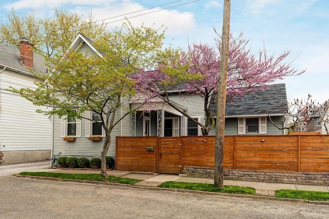 view of front of home with a fenced front yard, a gate, and a shingled roof