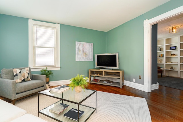 living room featuring built in shelves, baseboards, and wood finished floors