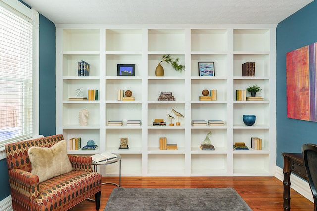 living area with a wealth of natural light, built in shelves, dark wood-style flooring, and a textured ceiling