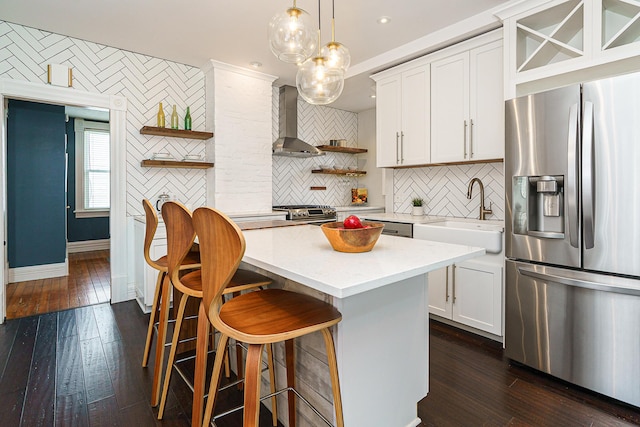 kitchen featuring open shelves, a sink, light countertops, stainless steel refrigerator with ice dispenser, and wall chimney exhaust hood