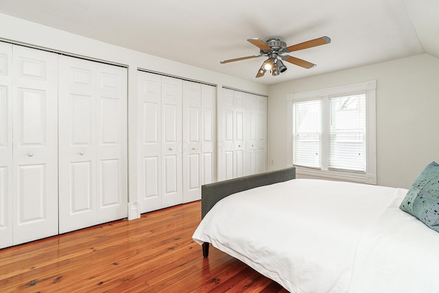 bedroom with ceiling fan, vaulted ceiling, two closets, and wood finished floors