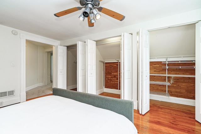 bedroom with wood finished floors, a ceiling fan, visible vents, baseboards, and two closets