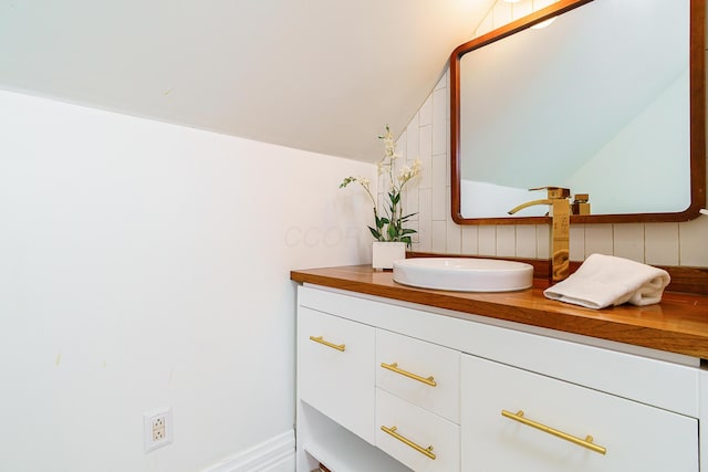 bathroom with lofted ceiling, vanity, and baseboards