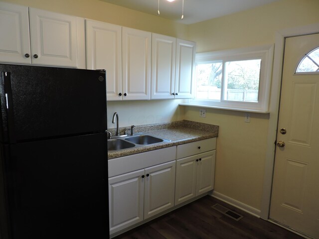 kitchen with white cabinets, black refrigerator, dark hardwood / wood-style flooring, and sink