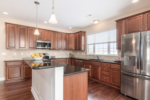 kitchen with sink, a center island, hanging light fixtures, dark stone countertops, and appliances with stainless steel finishes