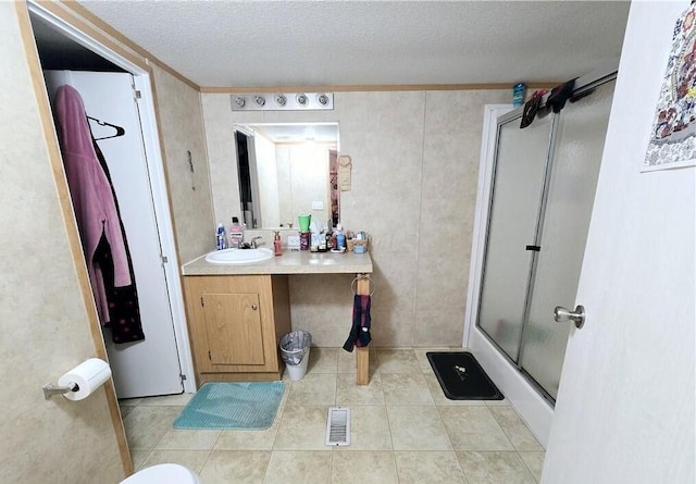 bathroom featuring vanity, a textured ceiling, walk in shower, and tile patterned flooring