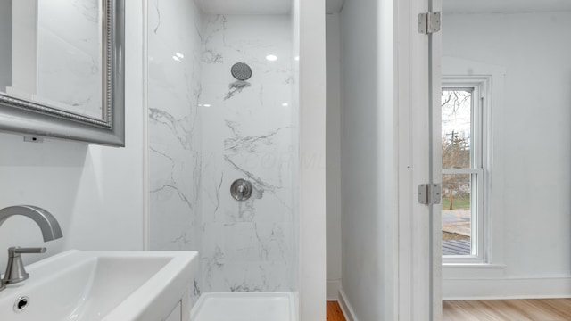 bathroom with a tile shower, sink, a wealth of natural light, and wood-type flooring