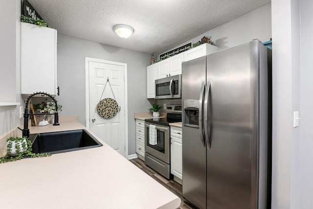 kitchen featuring white cabinetry, sink, dark wood-type flooring, stainless steel appliances, and a textured ceiling