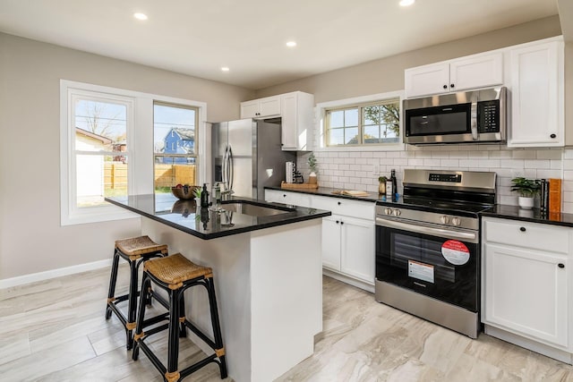 kitchen featuring white cabinets, stainless steel appliances, plenty of natural light, and a center island with sink