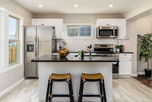 kitchen featuring tasteful backsplash, an island with sink, white cabinets, and stainless steel appliances