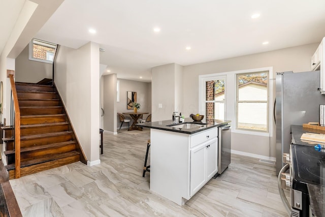 kitchen with sink, an island with sink, a breakfast bar area, white cabinets, and appliances with stainless steel finishes