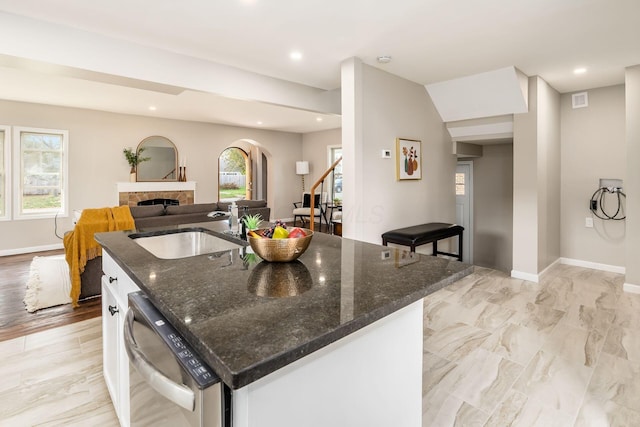 kitchen with white cabinetry, dishwasher, sink, dark stone countertops, and a kitchen island with sink