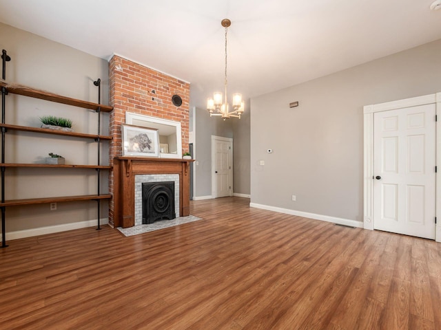 unfurnished living room featuring a chandelier, a brick fireplace, and wood-type flooring