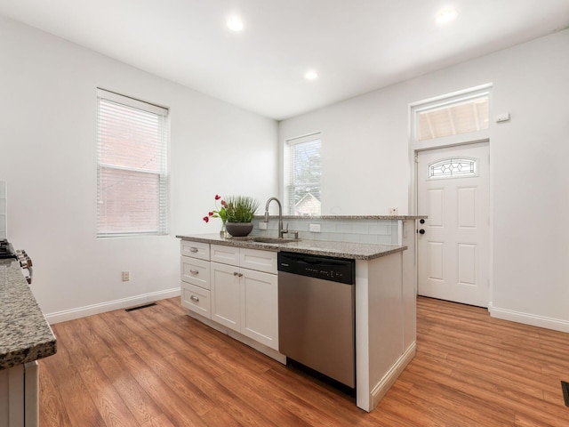 kitchen with light stone countertops, white cabinets, dishwasher, light hardwood / wood-style floors, and a center island with sink