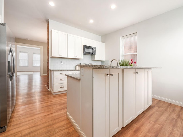 kitchen with stainless steel refrigerator with ice dispenser, white cabinetry, light hardwood / wood-style floors, and an island with sink