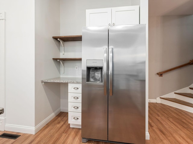 kitchen with white cabinets, light wood-type flooring, light stone countertops, and stainless steel fridge