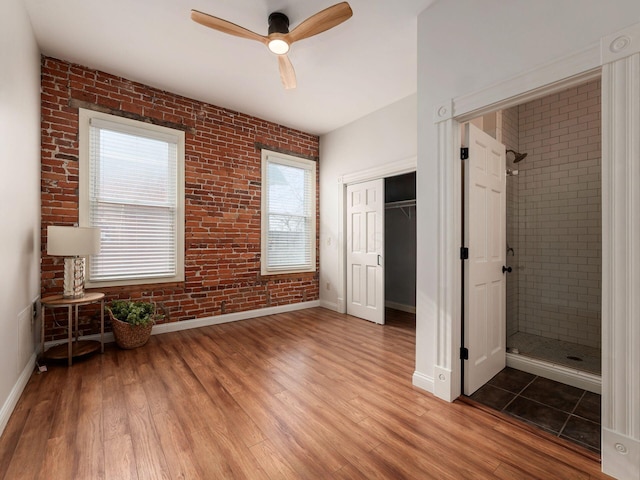 unfurnished bedroom featuring multiple windows, hardwood / wood-style flooring, brick wall, and ceiling fan