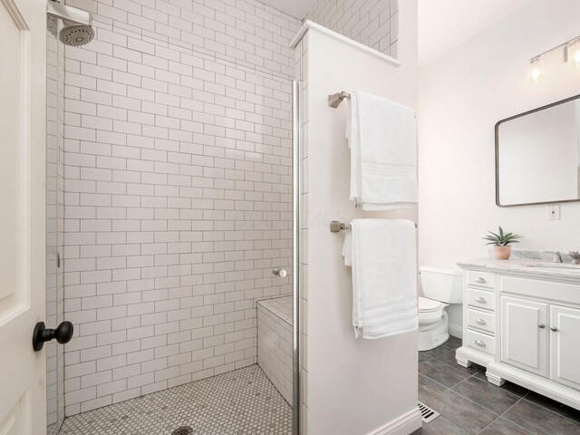 bathroom with vanity, toilet, a tile shower, and tile patterned flooring