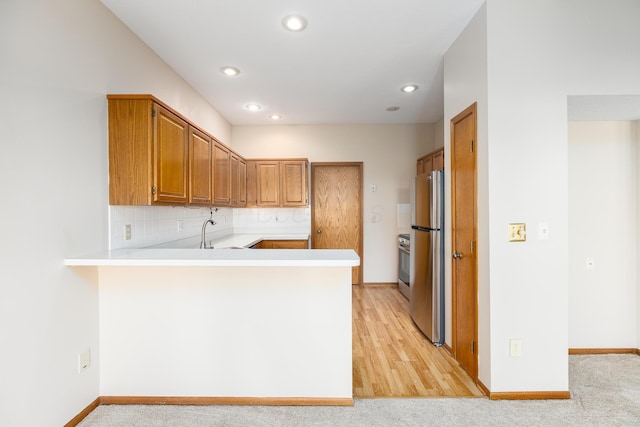 kitchen featuring kitchen peninsula, light wood-type flooring, tasteful backsplash, and stainless steel refrigerator