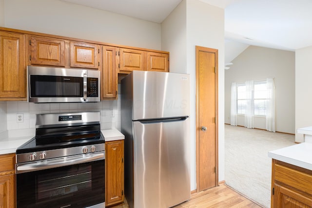 kitchen featuring stainless steel appliances, vaulted ceiling, tasteful backsplash, and light hardwood / wood-style flooring