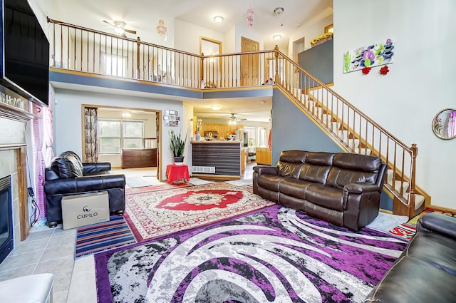 living room featuring a tile fireplace, a towering ceiling, ceiling fan, and light tile patterned flooring