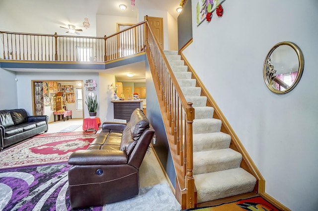 carpeted living room featuring ceiling fan and a towering ceiling