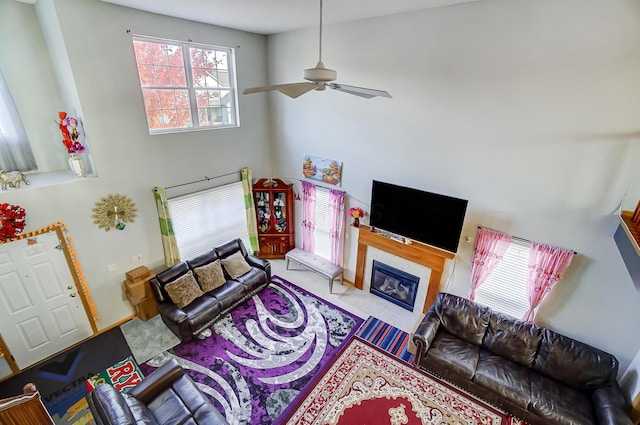 living room featuring ceiling fan, a fireplace, and a towering ceiling