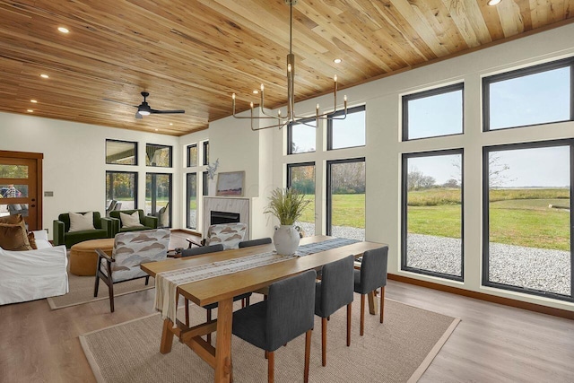 dining room with a high ceiling, ceiling fan with notable chandelier, light hardwood / wood-style floors, and wooden ceiling