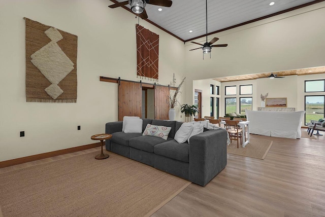 living room featuring light wood-type flooring, a barn door, high vaulted ceiling, and ceiling fan