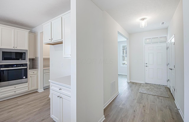 kitchen with built in microwave, stainless steel oven, white cabinets, and light hardwood / wood-style floors