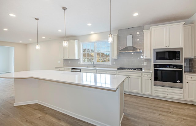 kitchen with wall chimney exhaust hood, sink, white cabinetry, a center island, and appliances with stainless steel finishes