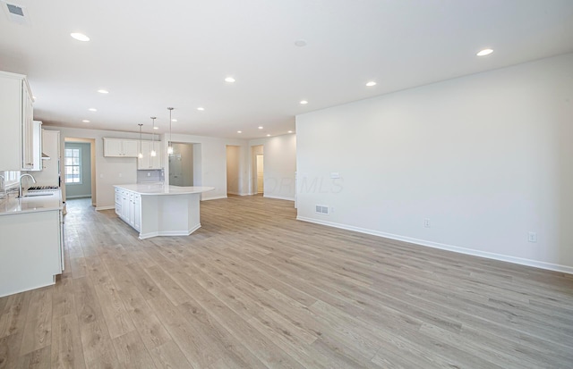 kitchen with a kitchen island, pendant lighting, white cabinetry, sink, and light hardwood / wood-style flooring