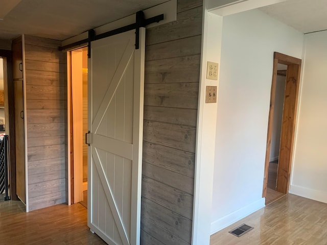 hallway with wood-type flooring, a barn door, and wooden walls