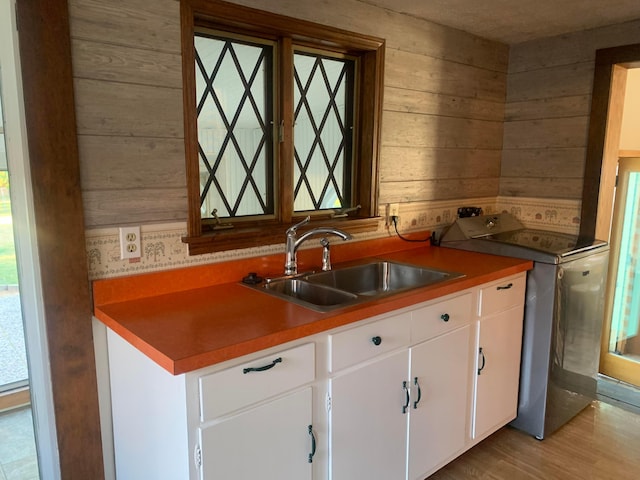 kitchen featuring white cabinetry, sink, light hardwood / wood-style floors, and wood walls