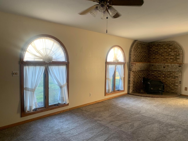 unfurnished living room with carpet floors, a wood stove, and ceiling fan