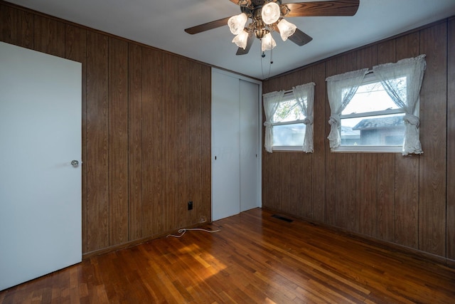 empty room with wood walls, ceiling fan, visible vents, and dark wood-style flooring