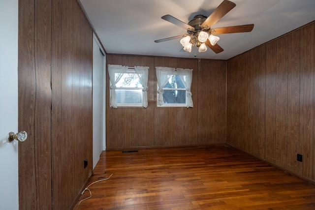 spare room with dark wood-style floors, visible vents, wood walls, and ceiling fan