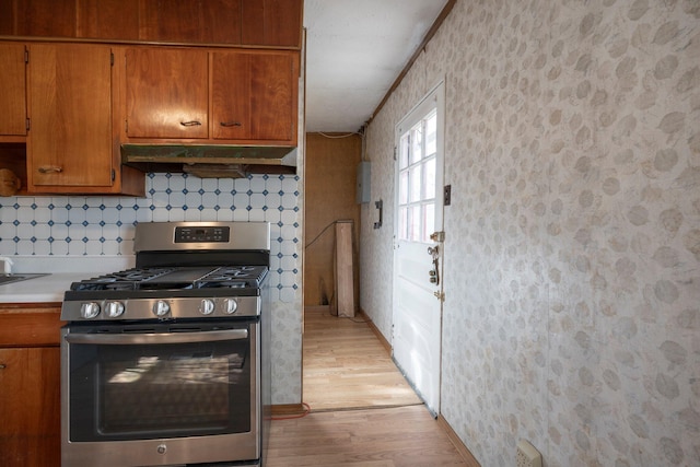 kitchen featuring under cabinet range hood, light countertops, light wood-type flooring, brown cabinets, and stainless steel gas stove