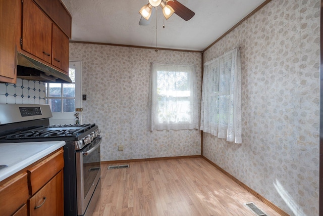 kitchen with wallpapered walls, under cabinet range hood, light countertops, and stainless steel range with gas stovetop