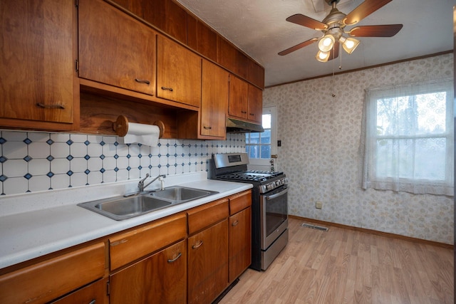 kitchen featuring light countertops, gas stove, a sink, and wallpapered walls