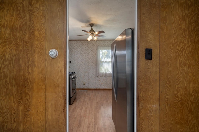 kitchen featuring appliances with stainless steel finishes, a ceiling fan, light wood-style floors, baseboards, and wallpapered walls