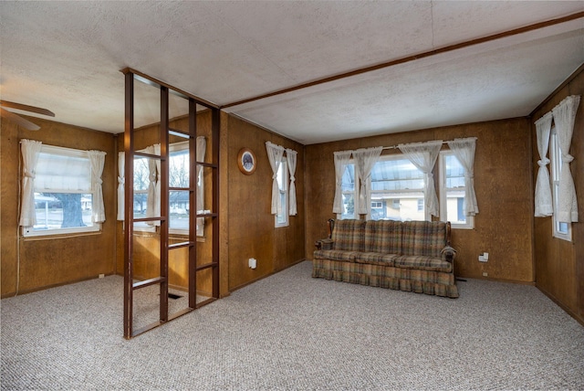 unfurnished living room with a textured ceiling, plenty of natural light, light colored carpet, and wooden walls