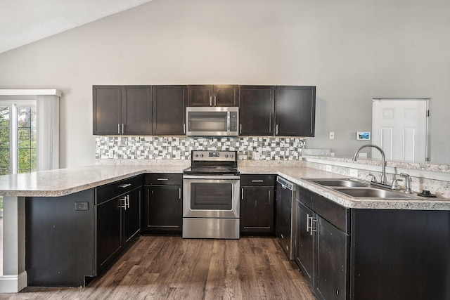 kitchen featuring kitchen peninsula, appliances with stainless steel finishes, backsplash, dark wood-type flooring, and sink