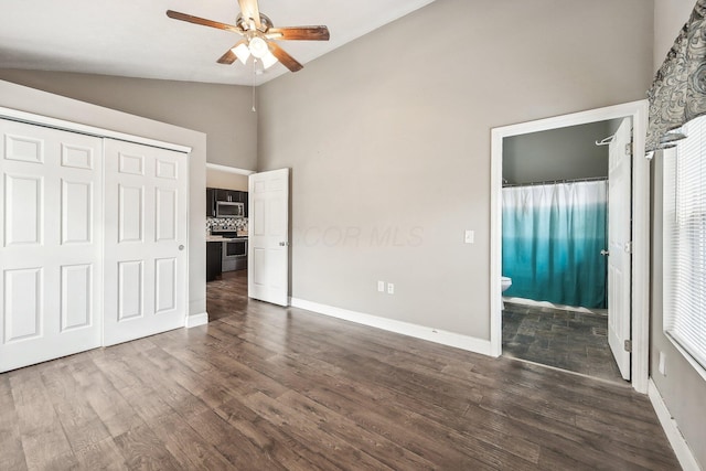 unfurnished bedroom featuring ensuite bath, ceiling fan, dark wood-type flooring, lofted ceiling, and a closet