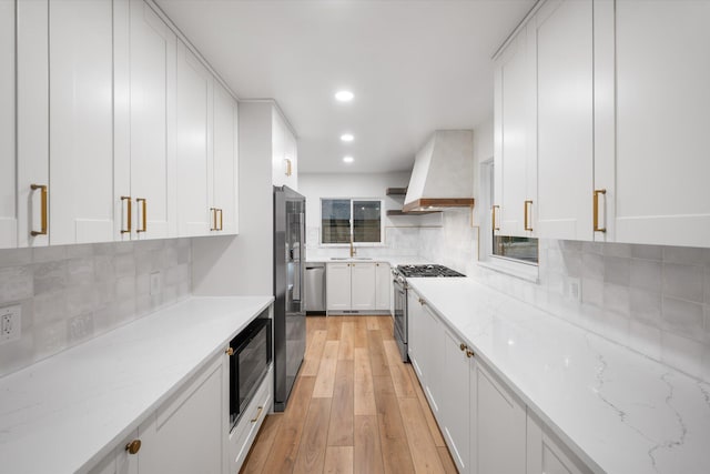 kitchen featuring premium range hood, white cabinets, appliances with stainless steel finishes, light hardwood / wood-style floors, and light stone counters