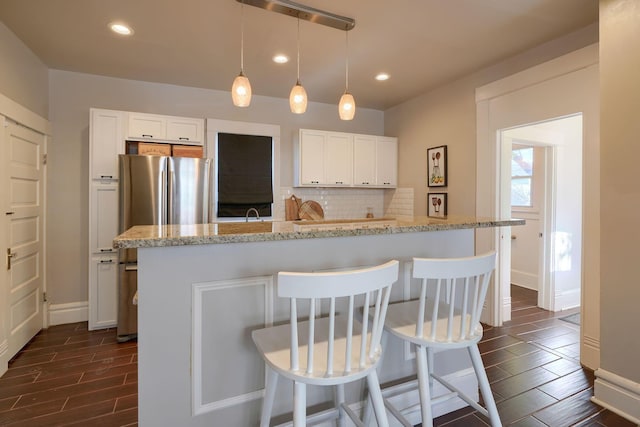 kitchen with white cabinetry, light stone counters, dark hardwood / wood-style flooring, a kitchen bar, and decorative backsplash